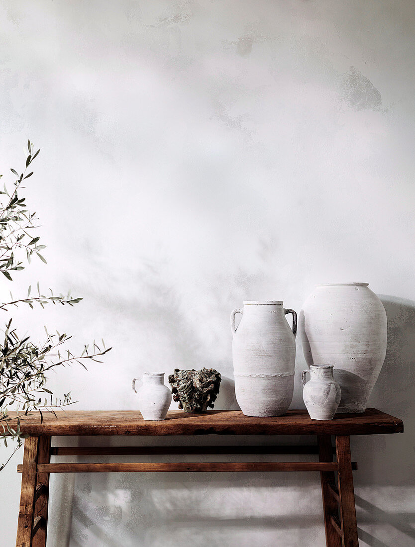 Rustikale Holzkonsole mit Vasen und Gefäßen neben Olivenbäumchen