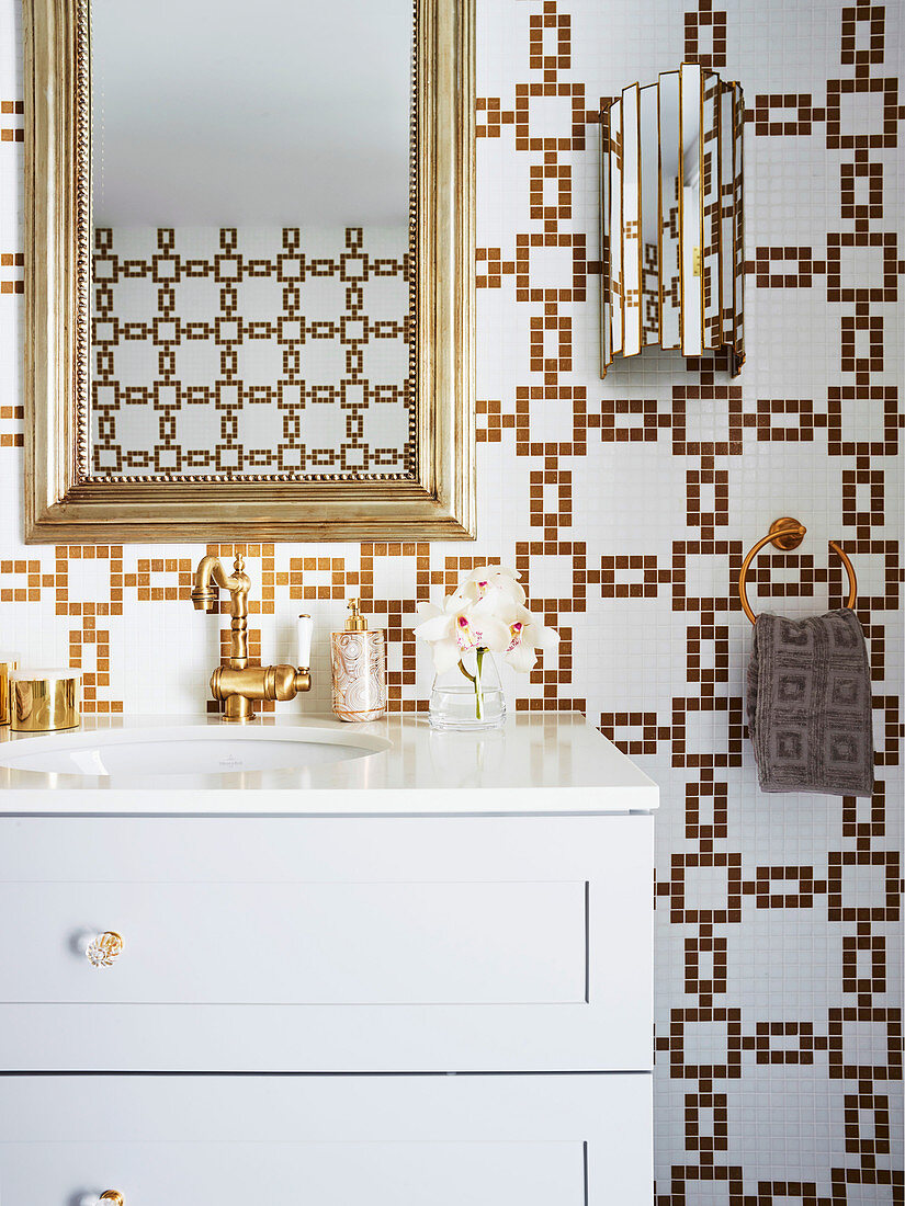Goldrahmenspiegel übe weißem Waschtisch in luxuriösem Badezimmer mit gold-weißen Mosaikfliesen