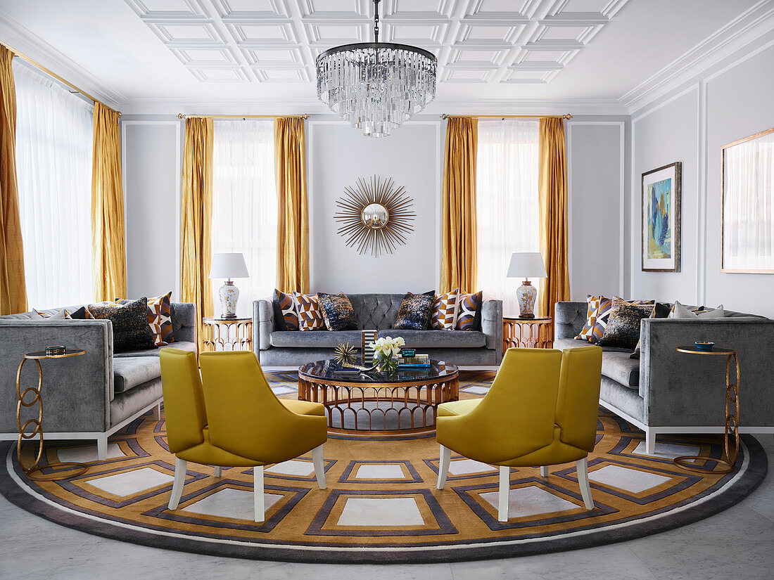 Gold-colored designer chairs and gray sofas with velvet upholstery around a marble table in a luxurious living room