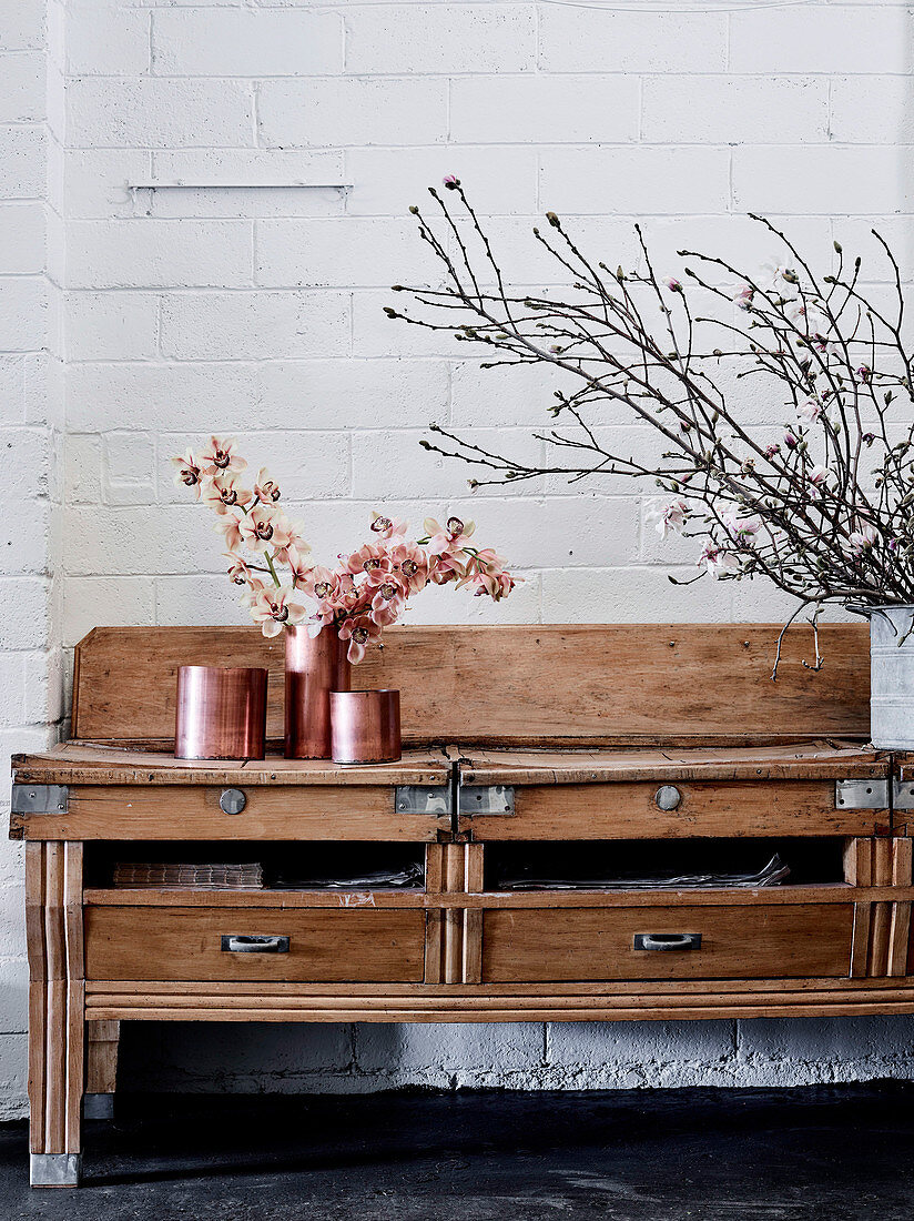 Old wooden table with drawers and vessels in rose gold with orchid flowers