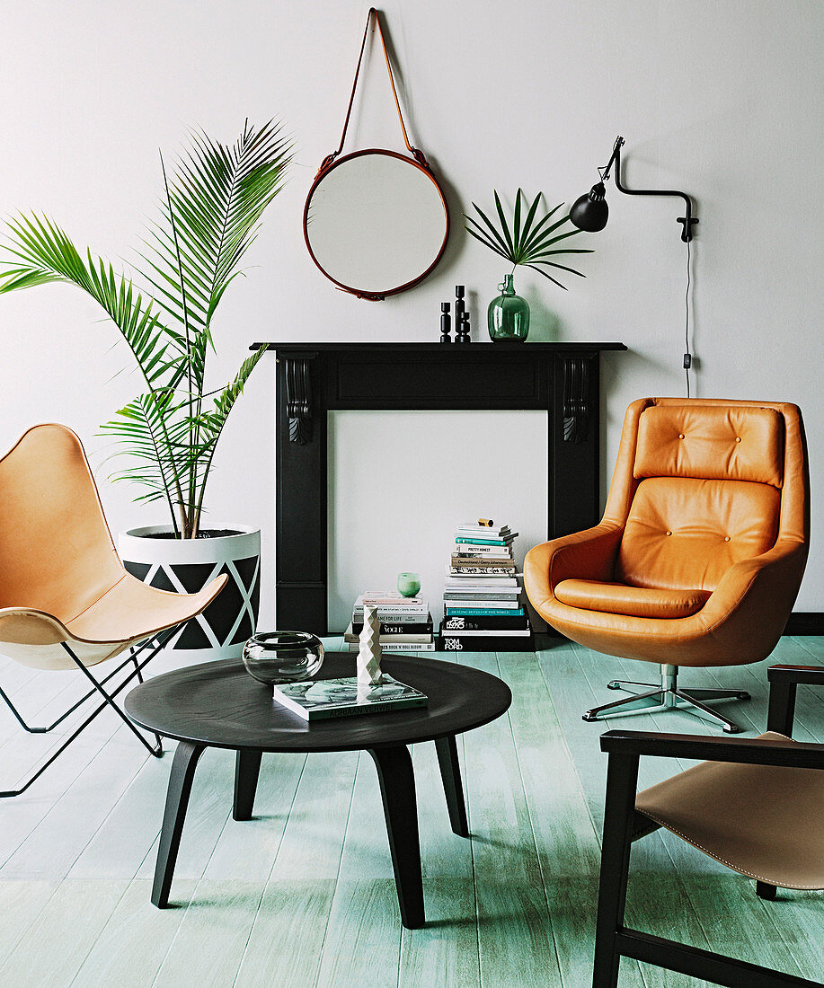 Cognacfarbene Sitzmöbel vor Kamin-Attrappe, Coffeetable und Zimmerpflanzen im Wohnzimmer