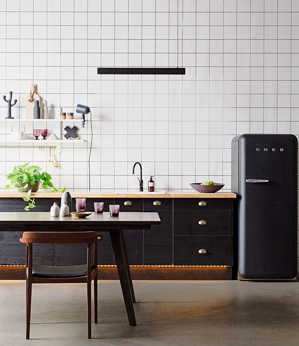 Schwarze Küchenzeile und schwarzer Kühlschrank vor Tapete mit Gittermuster, Esstisch und Stul