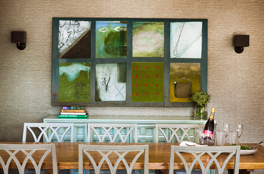 Esstisch mit Stühlen, dahinter Anrichte und Patchwork-Bild an tapezierter Wand