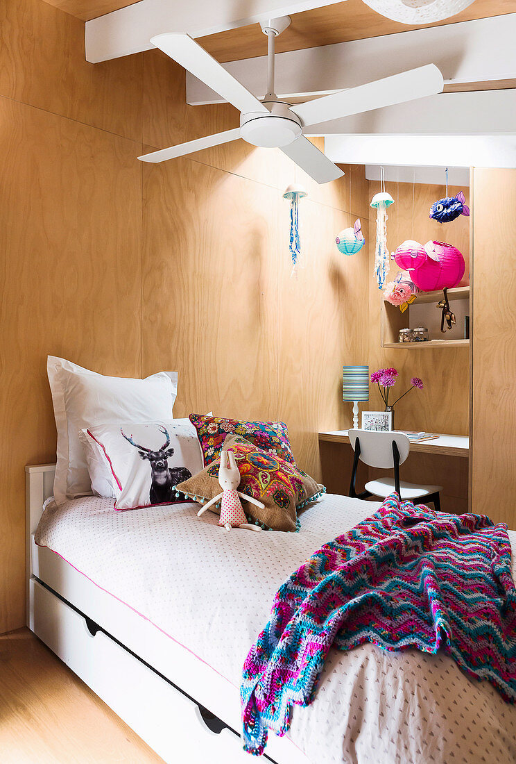 Bed under ceiling fan in girl's room with wooden paneling