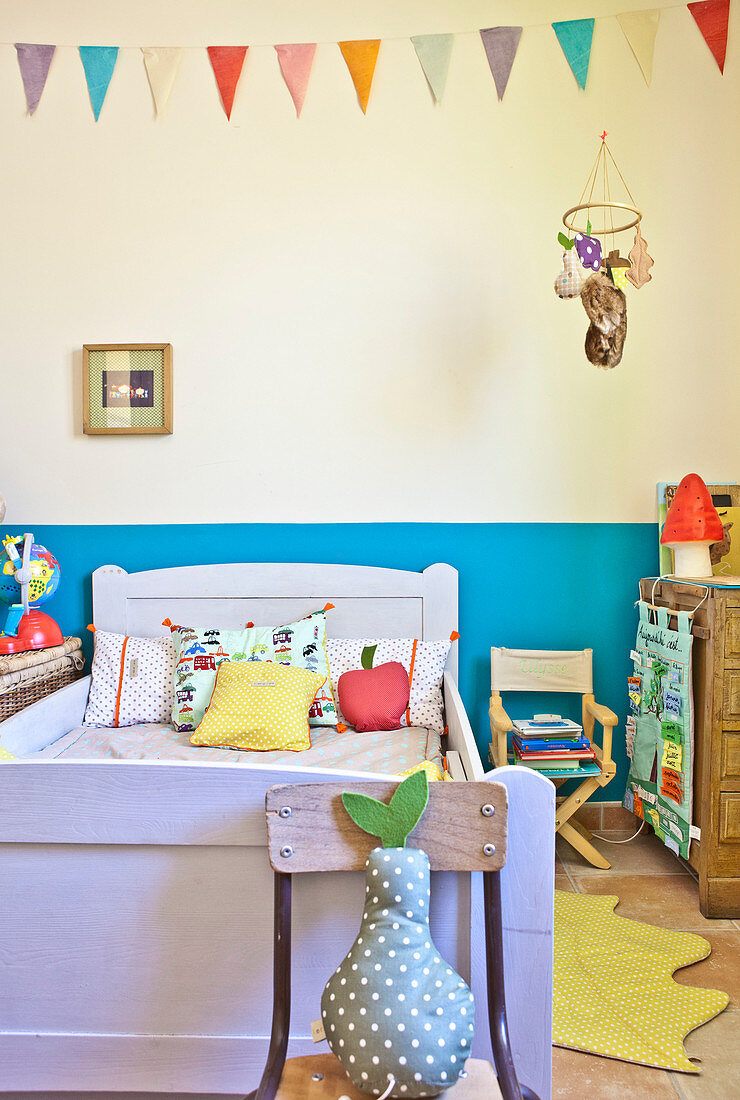 Colourful scatter cushions on wooden bed below bunting in child's bedroom