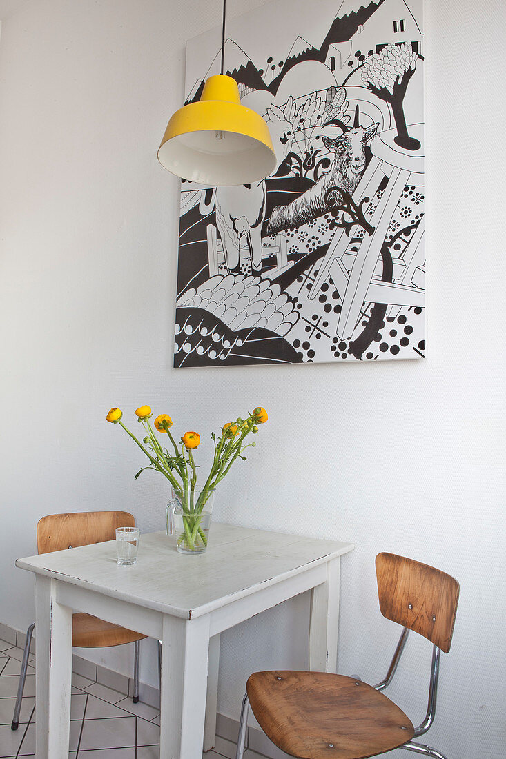 Small table and two chairs below yellow pendant lamp