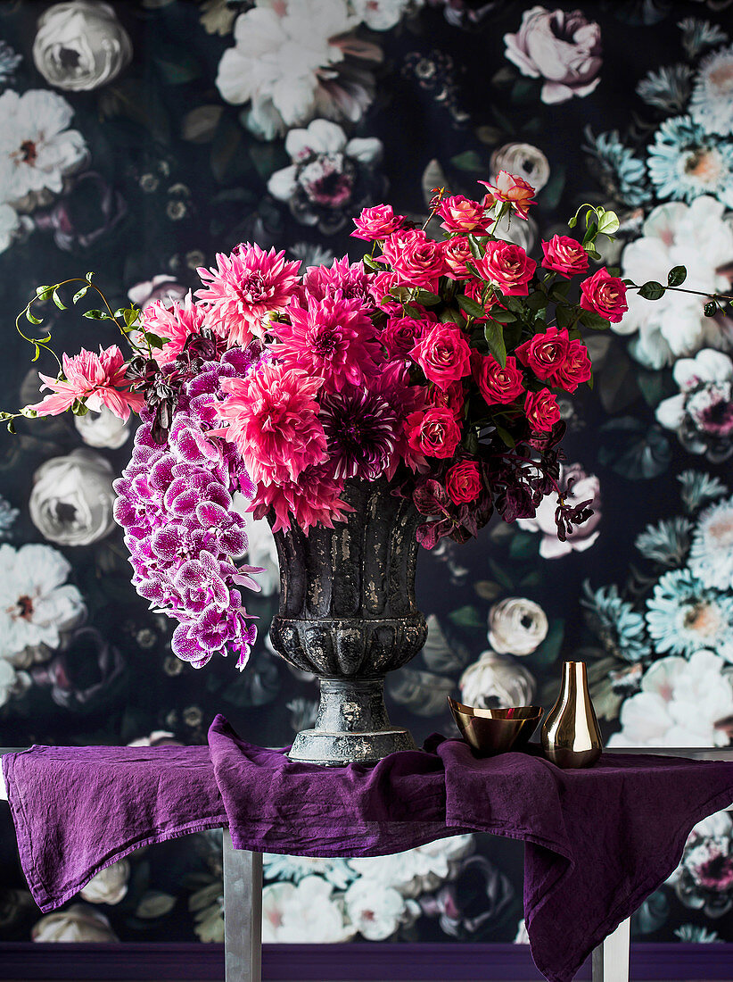 Opulent bouquet of flowers in an amphora in front of floral wallpaper