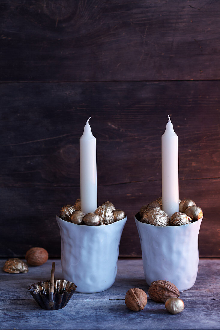 Porzellanbecher gefüllt mit goldfarbenen Nüssen als weihnachtliche Kerzenhalter