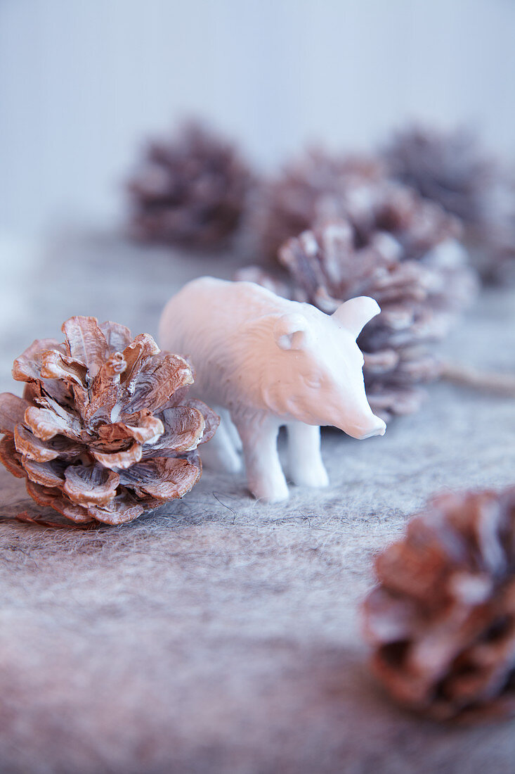 White wild boar figurine amongst pine cones on felt surface