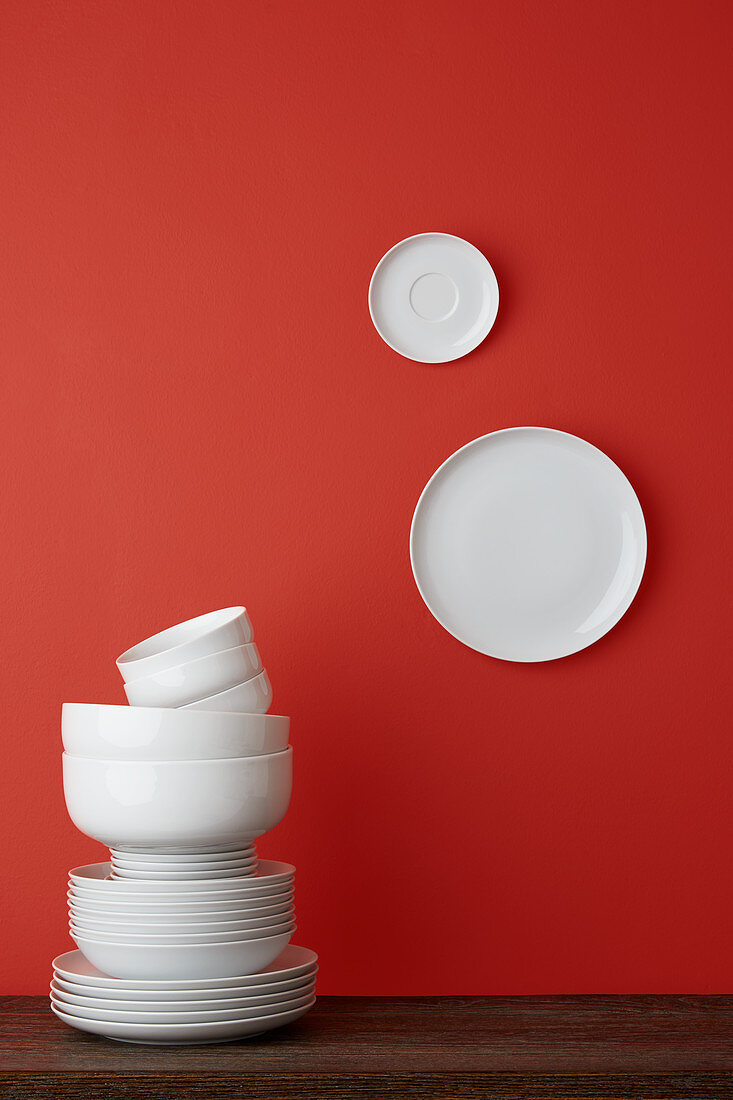 Gestapeltes weißes Geschirr und zwei Teller an roter Wand