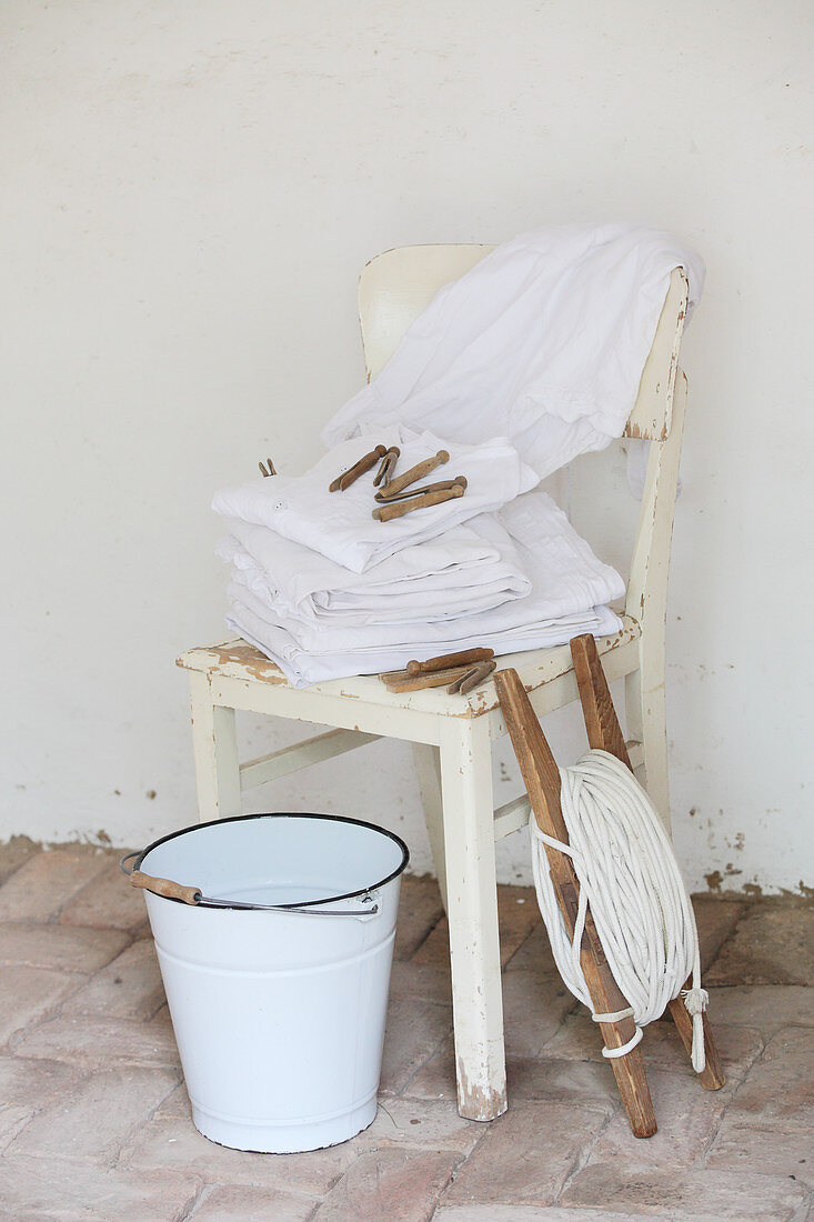 Nostalgische Wäschestücke fertig getrocknet auf Holzstuhl, daneben Wäscheleine und Emailleeimer