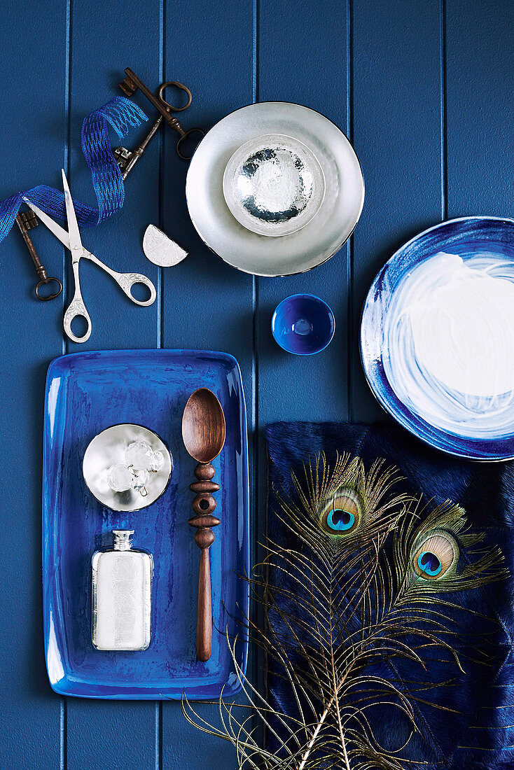 Bowls, pillows with peacock feathers and tray with wooden spoons and flacon on blue table