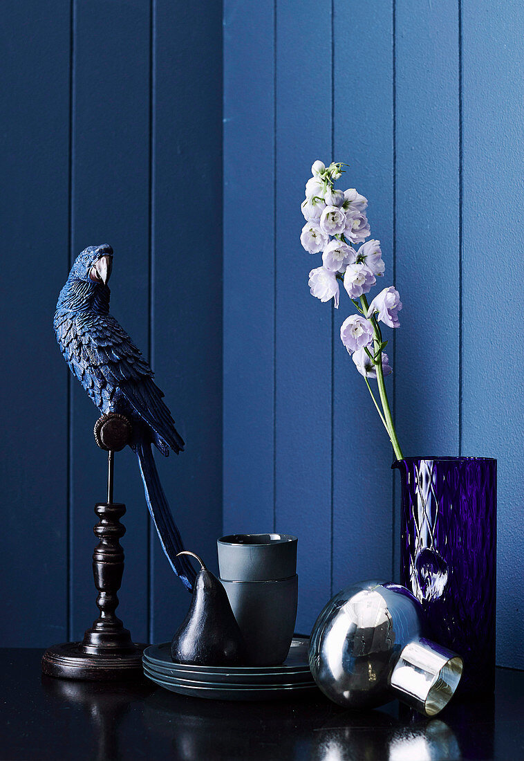 Decorative bird, crockery and glass vase with flower against blue wall