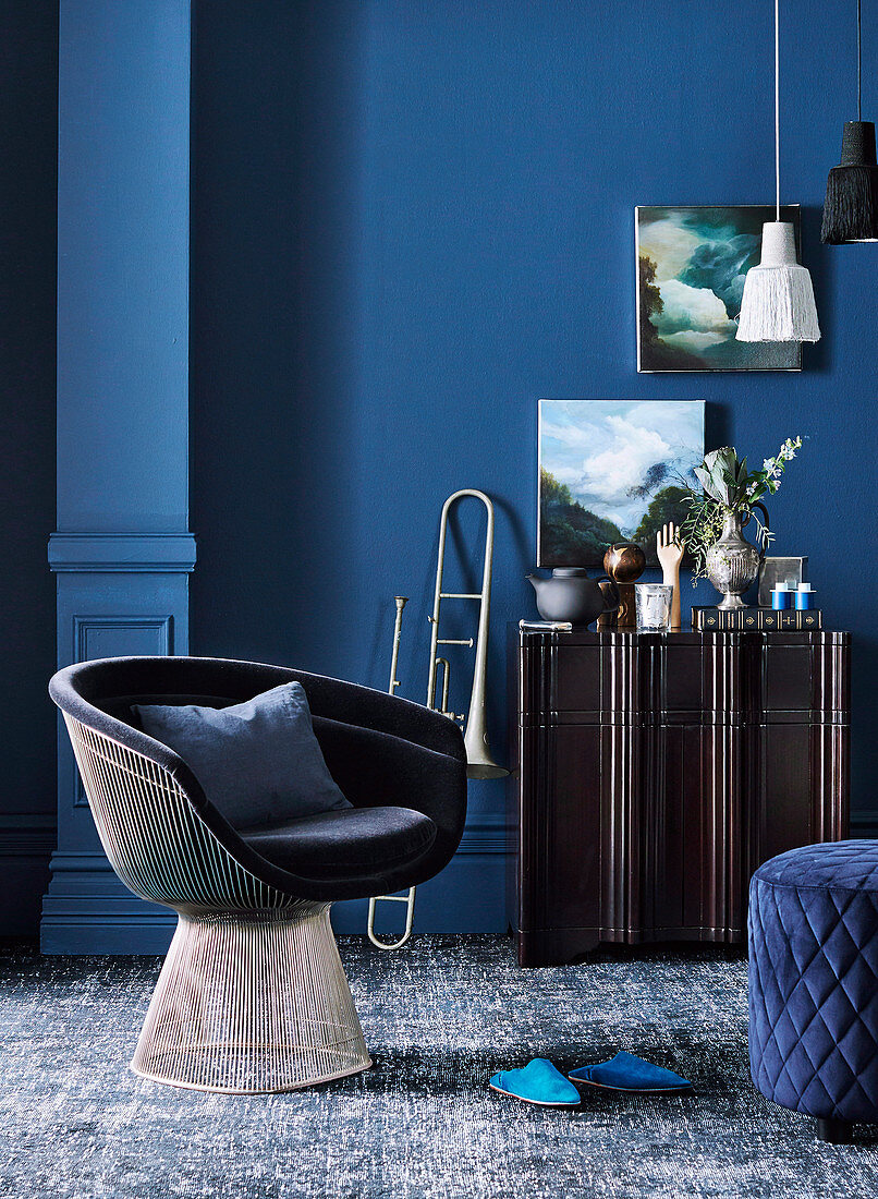 Classic lounge armchair, trumpet next to Siedeboard against blue wall in living room