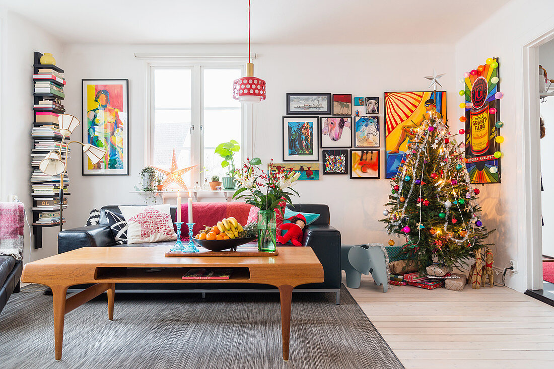 Couchtisch vor schwarzem Ledersofa im Wohnzimmer mit Weihnachtsbaum und mit Comics an der Wand