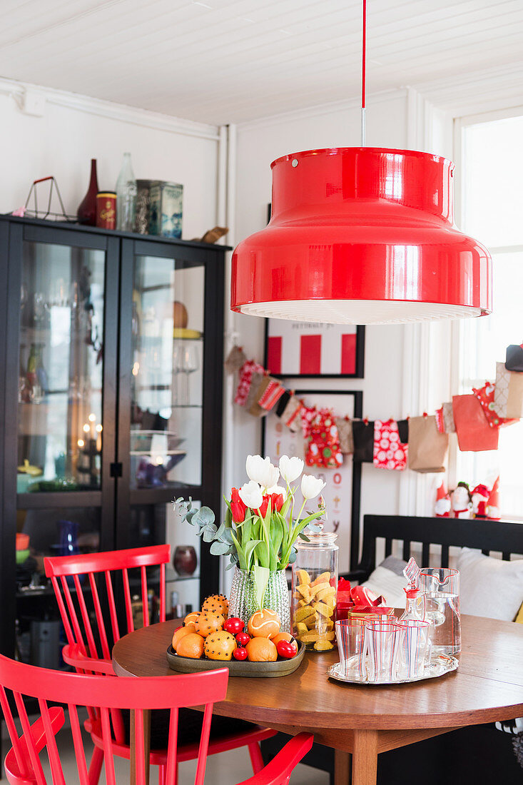Runder Tisch mit Weihnachtsdekoration, darüber roter Lampenschirm