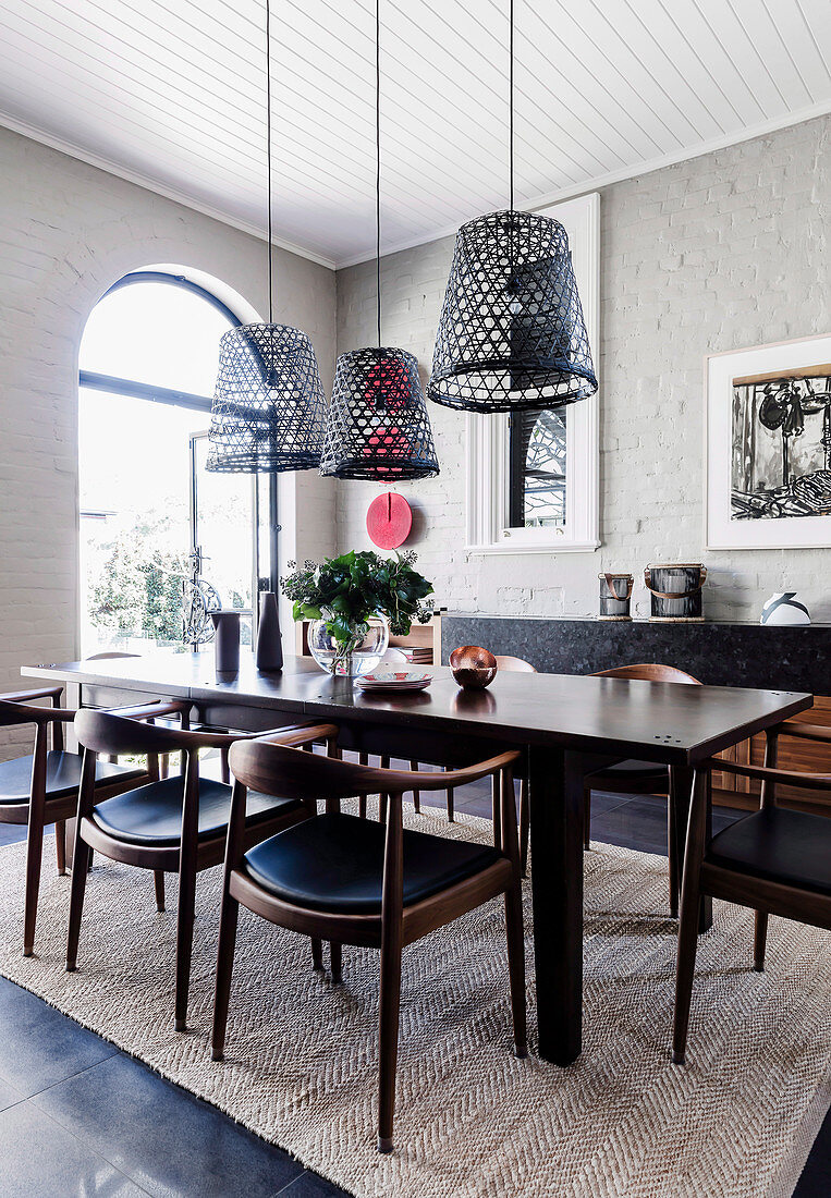 Dunkler Esstisch mit Stühlen, darüber Hängelampen aus alten Fischerkörben im Zimmer mit weiß gestrichener Ziegelwand