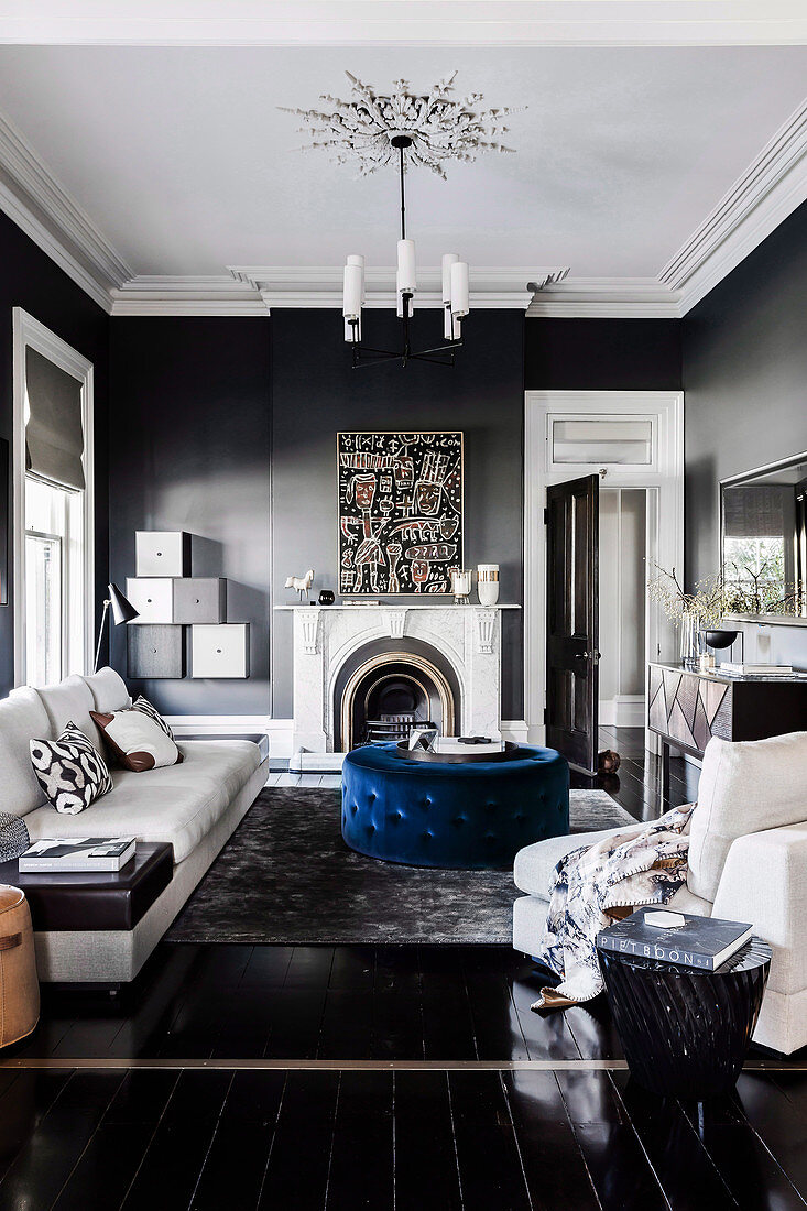 Helle Sofagarnitur, blauer Polstertisch und Kamin im Wohnzimmer mit dunkelgrauen Wänden und schwarzem Dielenboden