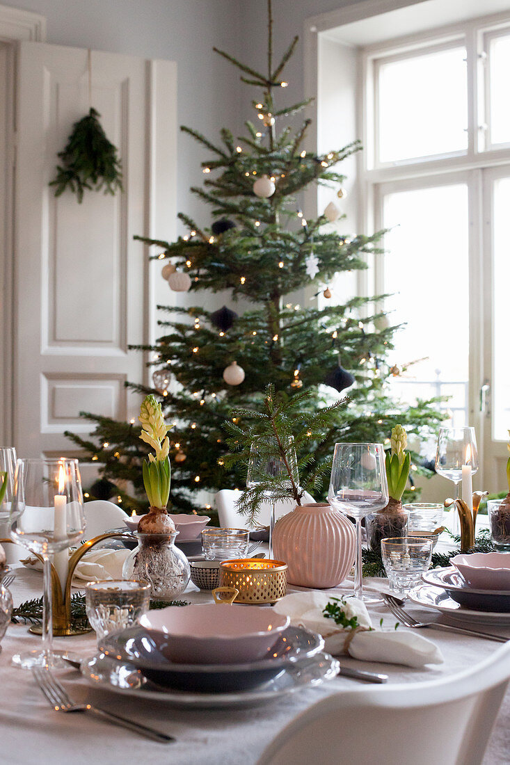 Festively set dining table in front of Christmas tree