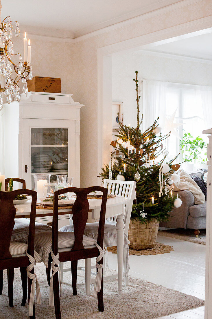 Weihnachtlich dekorierter Esstisch, Vitrinenschrank und geschmückter Weihnachtsbaum in skandinavischem Esszimmer