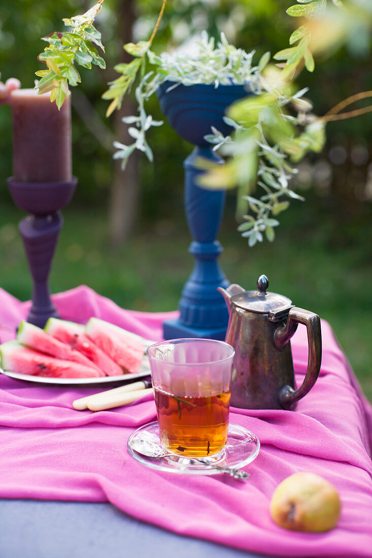 Teeglas, Melonen und bemalte Pokale auf dem Tisch im Garten