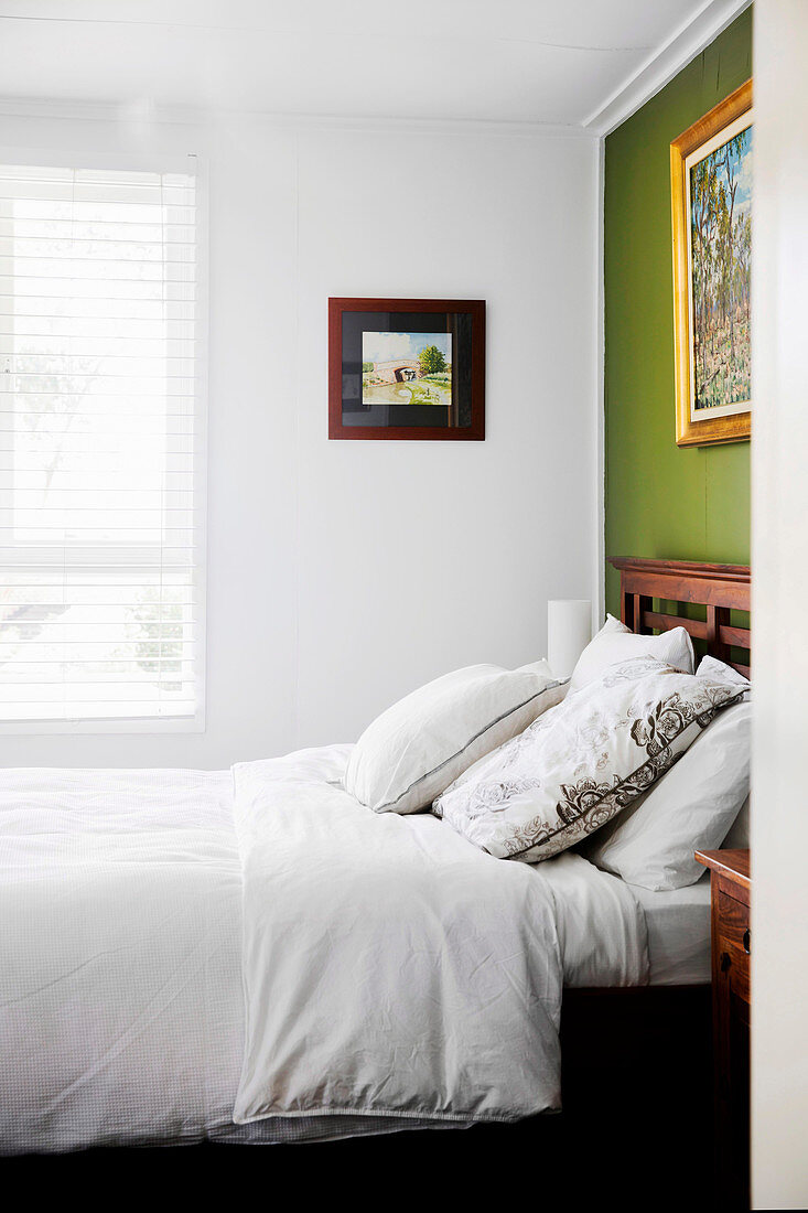 Doppelbett mit Betthaupt aus Holz an grüner Wand im Schlafzimmer