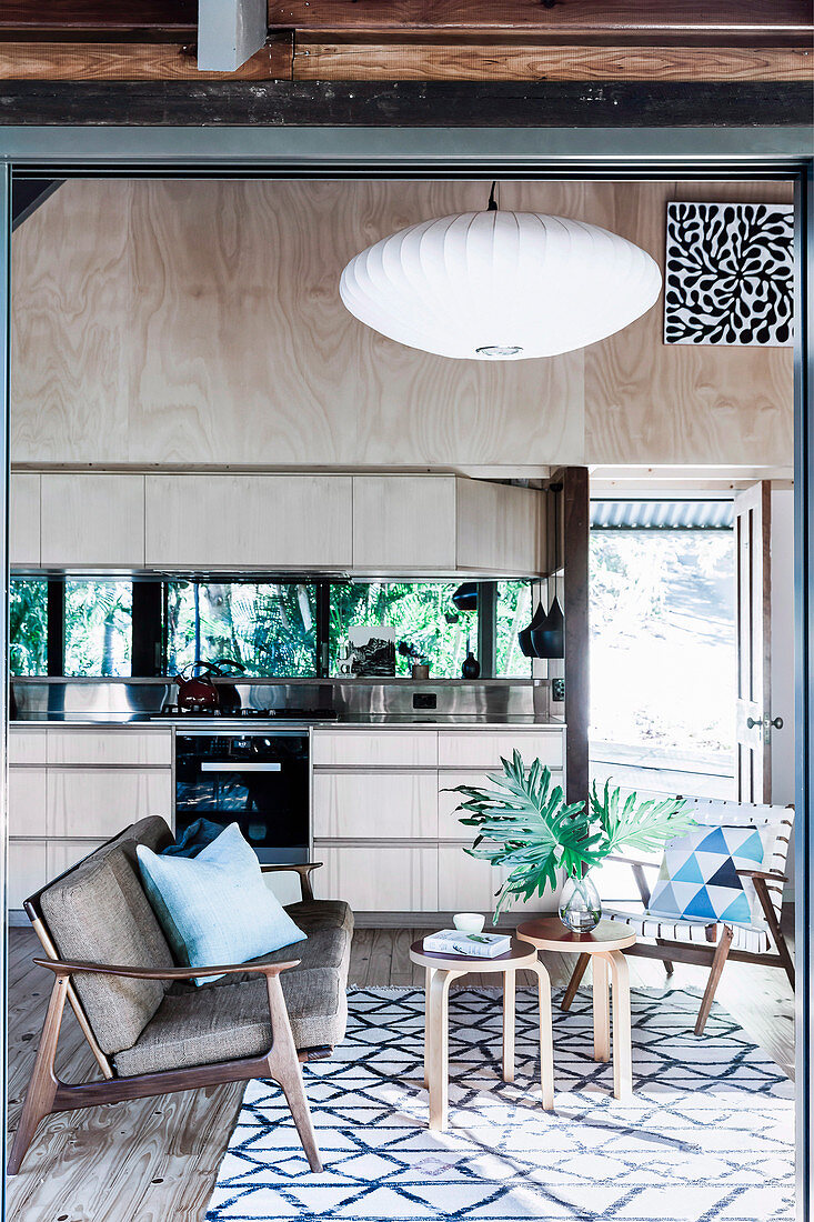 Offene Küche mit heller Holzfront und verspiegelter Rückwand, im Vordergrund Sitzbereich