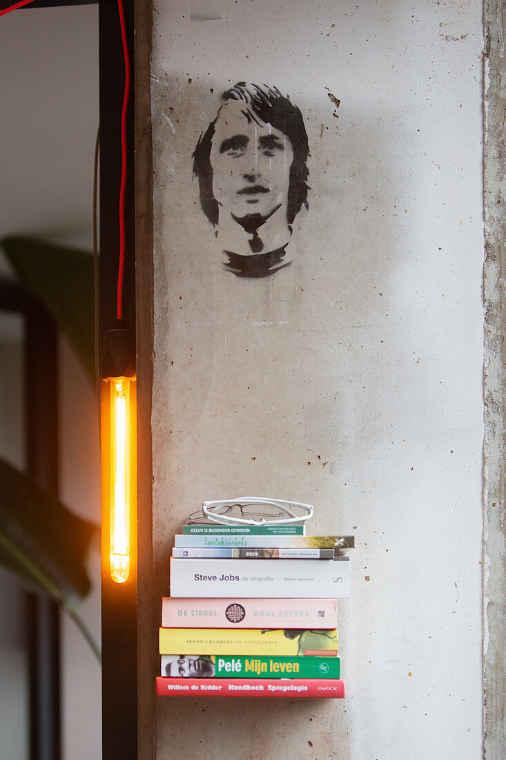Wandregal mit Bücherstapel, Leuchte und Portrait an der Wand