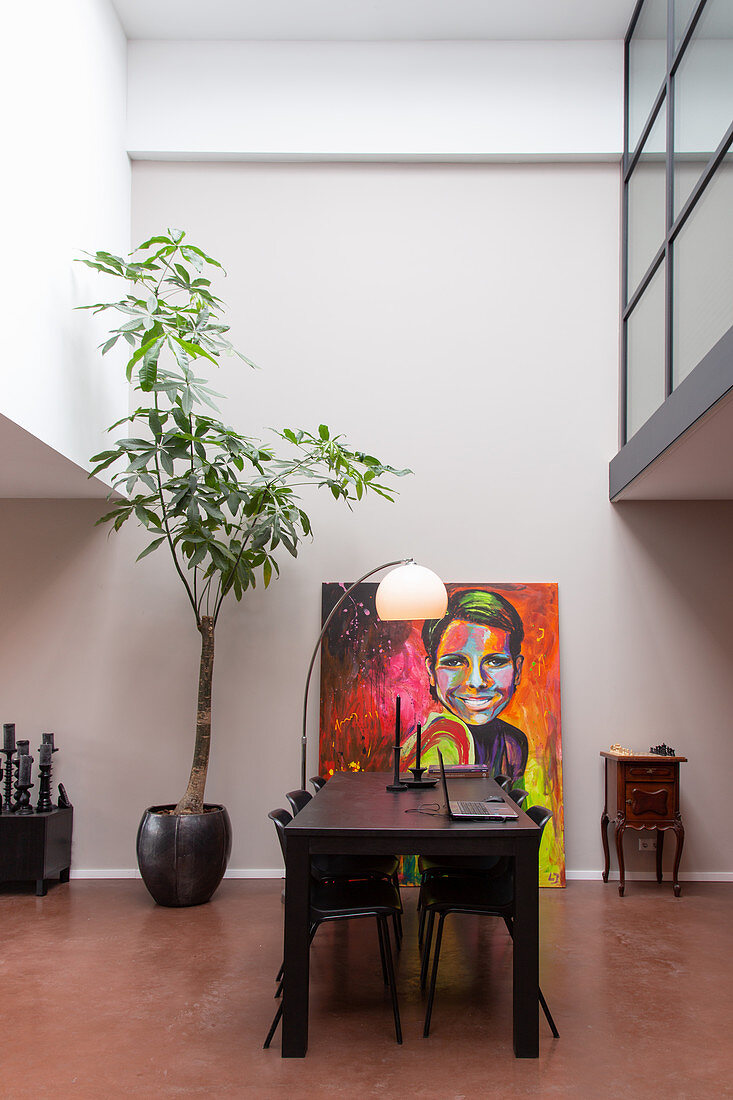 Dunkler Holztisch mit Stühlen, Stehleuchte, großformatiges Gemälde und Zimmerbäumchen in hohem Wohnraum