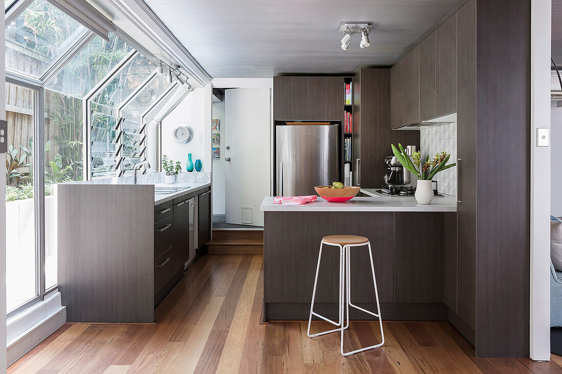 Elegante, dunkle Einbauküche mit Frühstückstheke, Edelstahl-Kühlschrank und Fensterfront