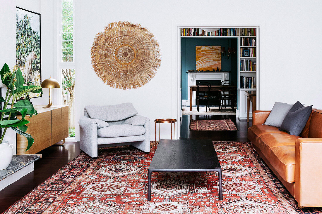 Sideboard, Polstersessel, Ledercouch und Couchtisch im Wohnzimmer, Blick durch offenem Durchgang auf Bücherregal und Essbereich