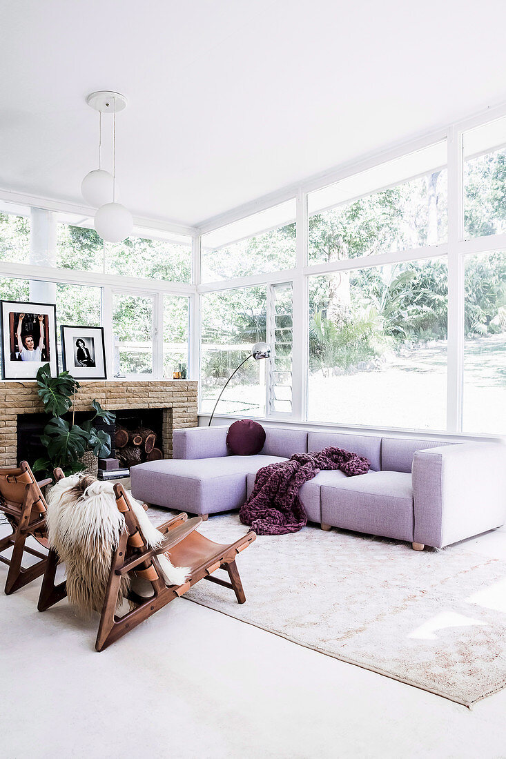 Lilafarbenes Sofa im Wohnzimmer mit umlaufender Fensterfront