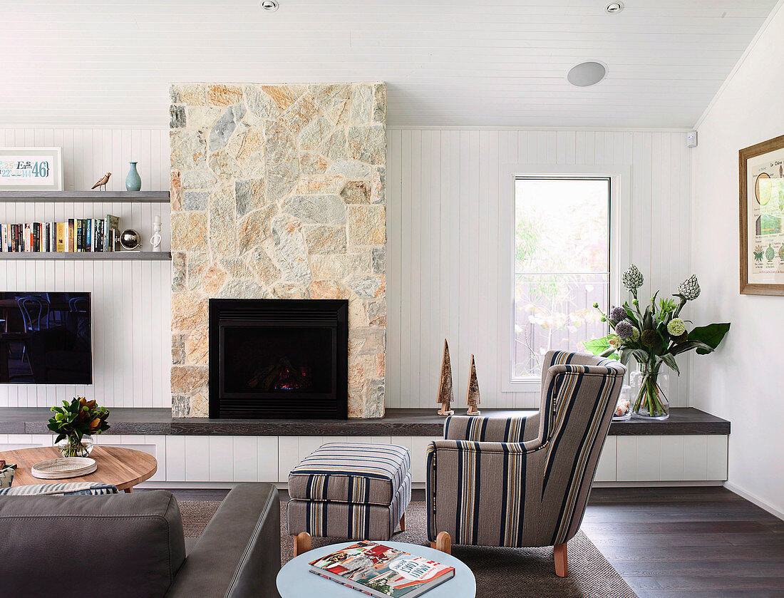 Living room with upholstered armchair, built-in bench and fireplace in sandstone wall
