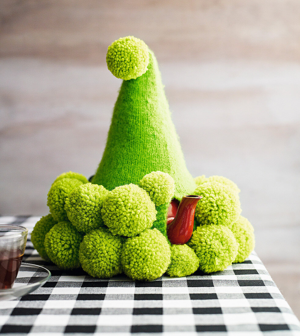 Green knitted hat with pompoms as a teapot warmer