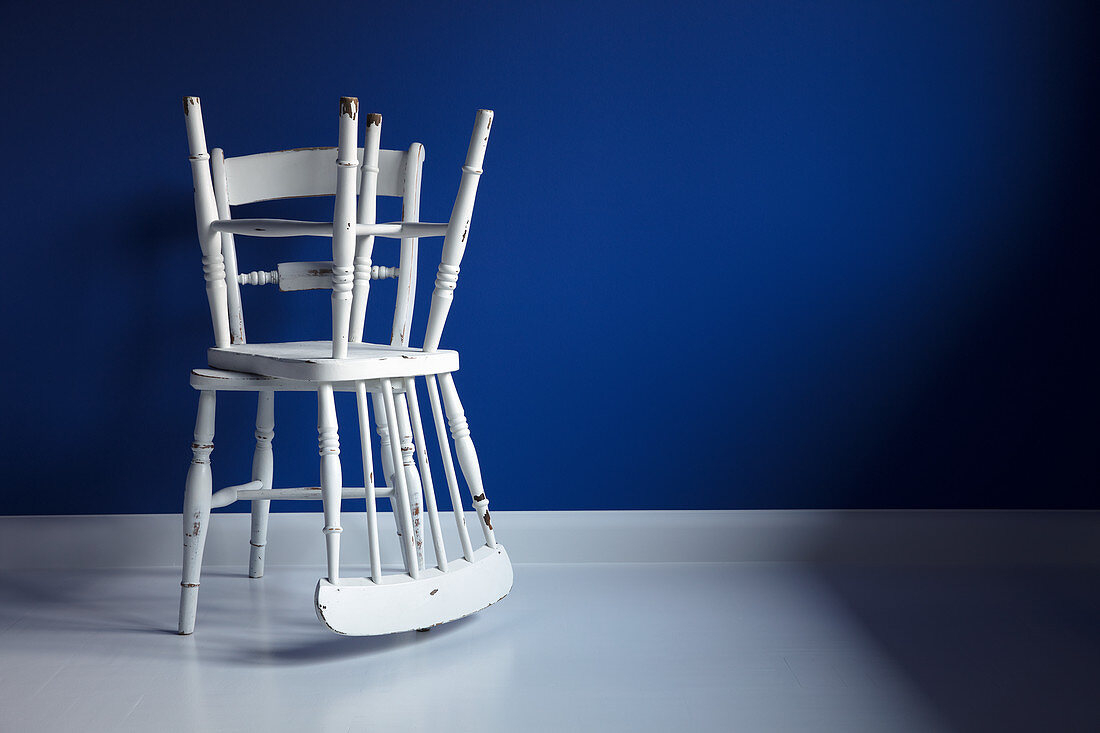Two battered white Windsor chairs against blue wall