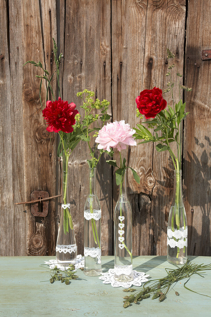 Peonies in glass bottles with lacy paper trim