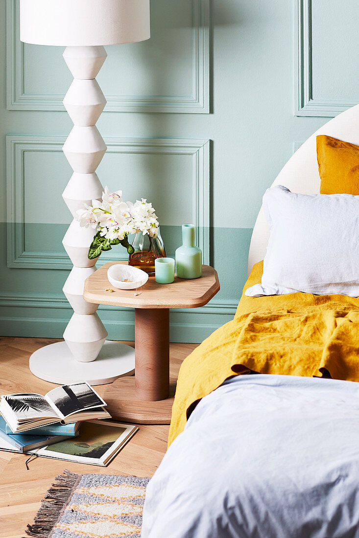 Bedside table and white floor lamp against mint green wall in bedroom