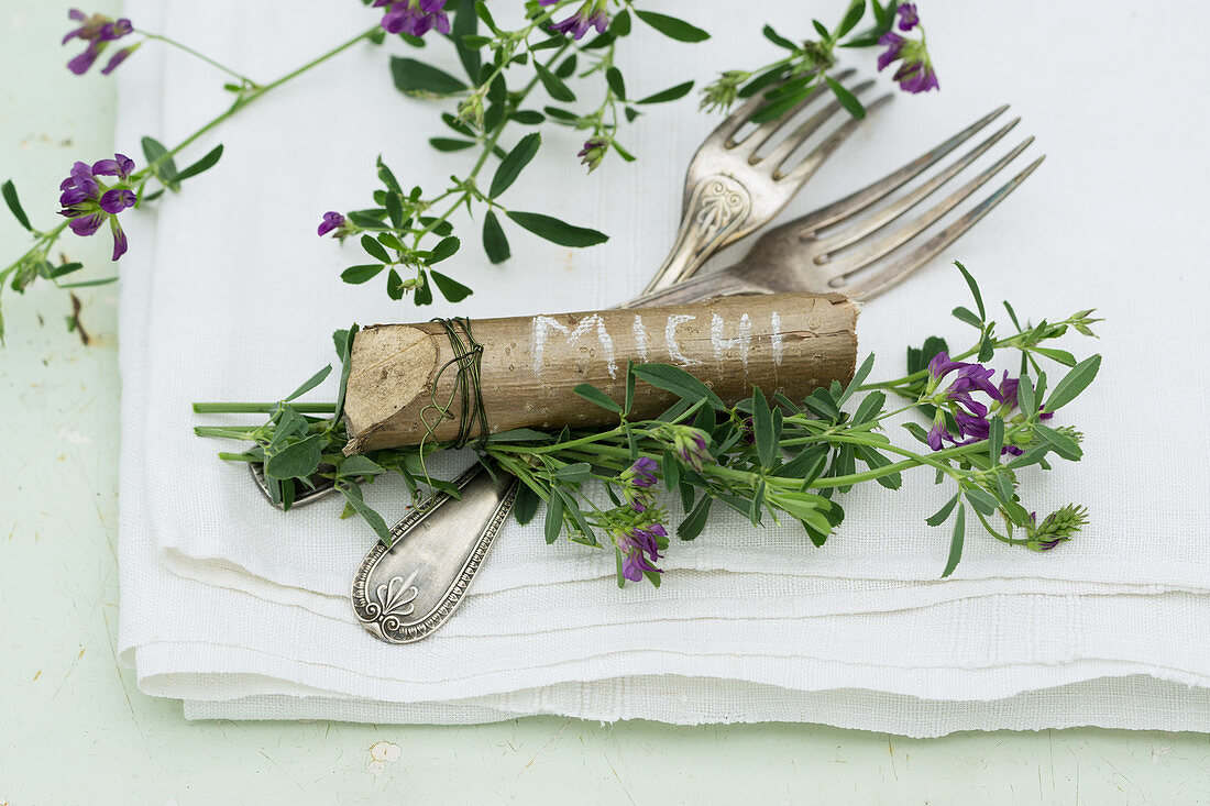 Cutlery and place markers made from pieces of hazel wood decorated with purple-flowering alfalfa (Medicago sativa)