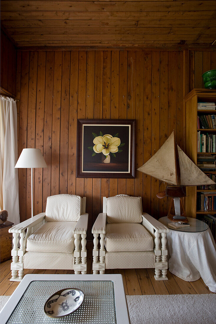 Two white armchairs against brown board wall in living room