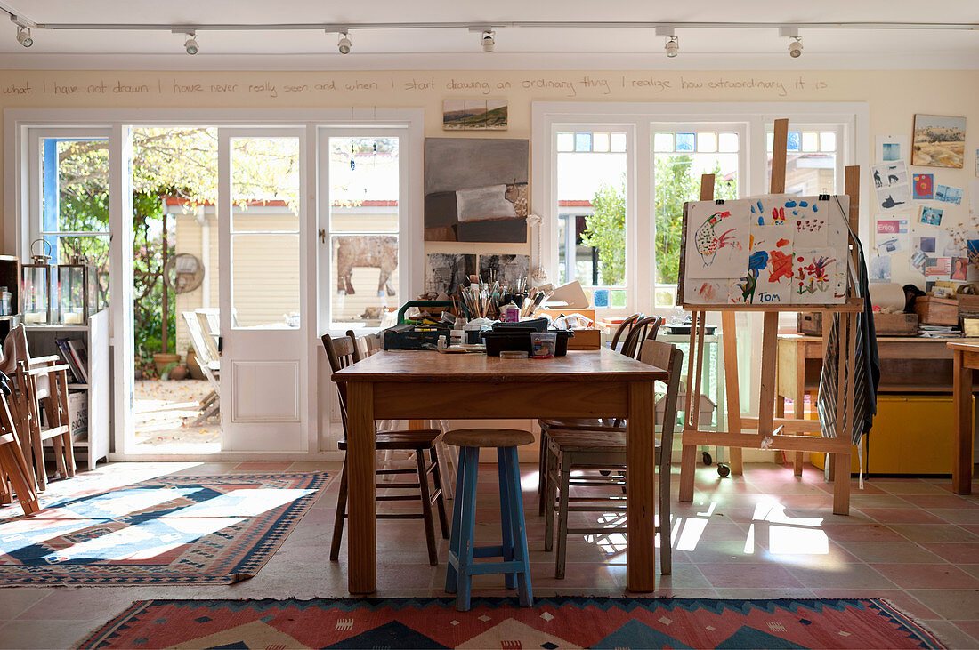 Holztisch und Staffelei im sonnigen Atelier mit Fenstern zum Hof