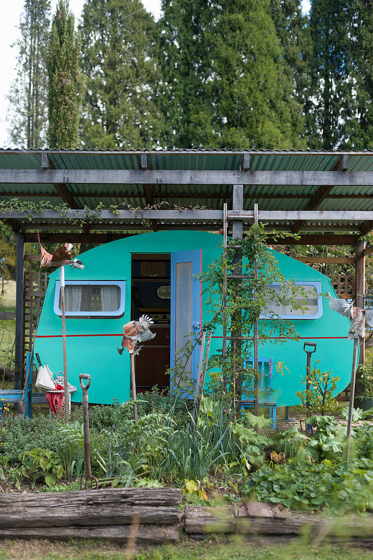 Green caravan below corrugated metal roof in garden