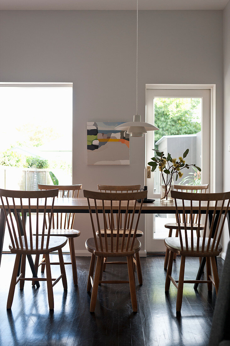 Spoke-back chairs around wooden table in dining room with garden access