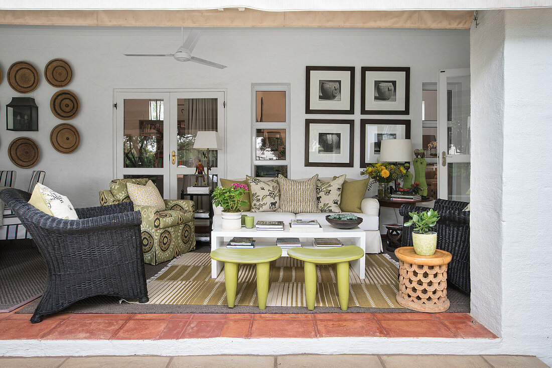 Blick auf wohnlich eingerichtete Veranda mit Sofa, Sesseln und grünen Senufo-Hockern