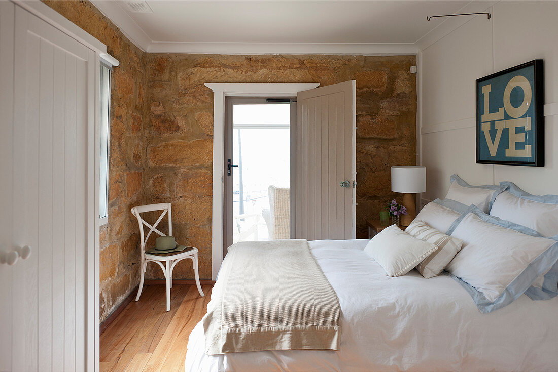 Doppelbett, darüber gerahmtes Plakat im Schlafzimmer mit Natursteinwand