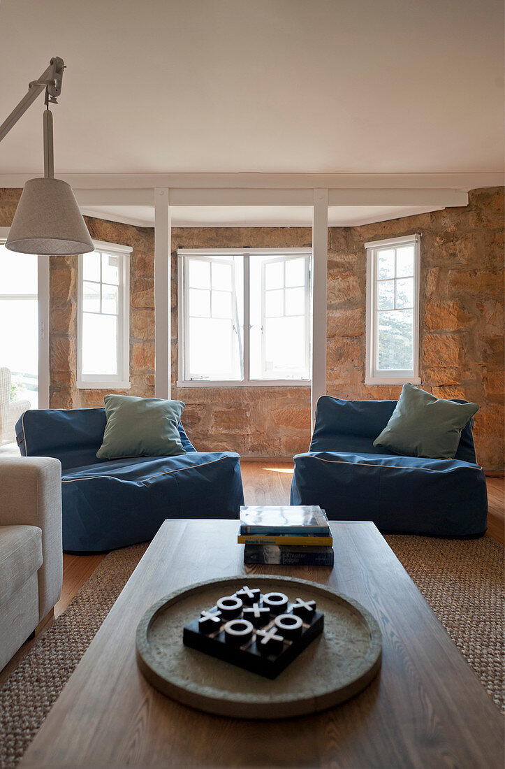 Große Sitzsäcke mit blauem Bezug und Couchtisch im Wohnzimmer mit Erker und Natursteinwand