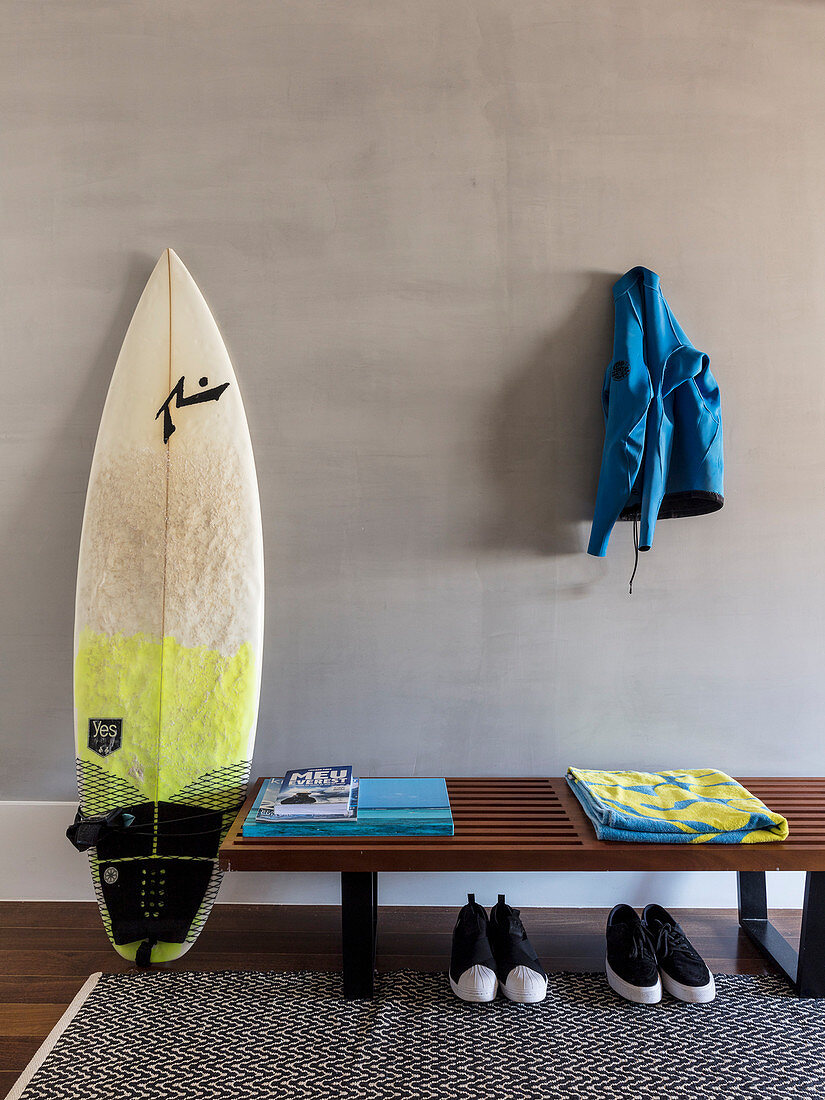 Surfboard next to wooden bench with pairs of shoes below