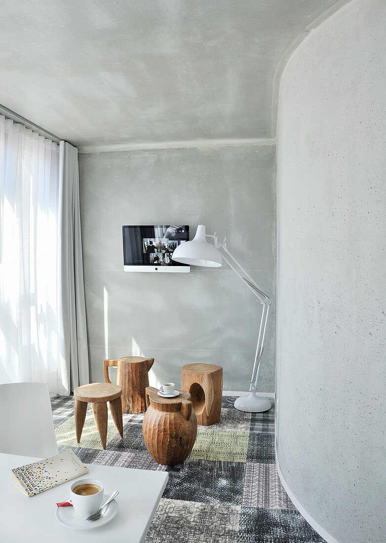 Tree-stump stools or various types and standard lamp in room with grey walls