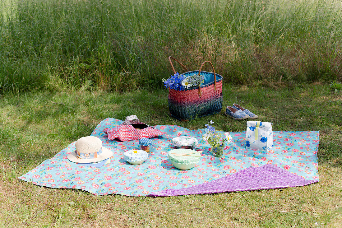 Bowls with lids, cake in bag and lunch bag on oilcloth picnic blanket