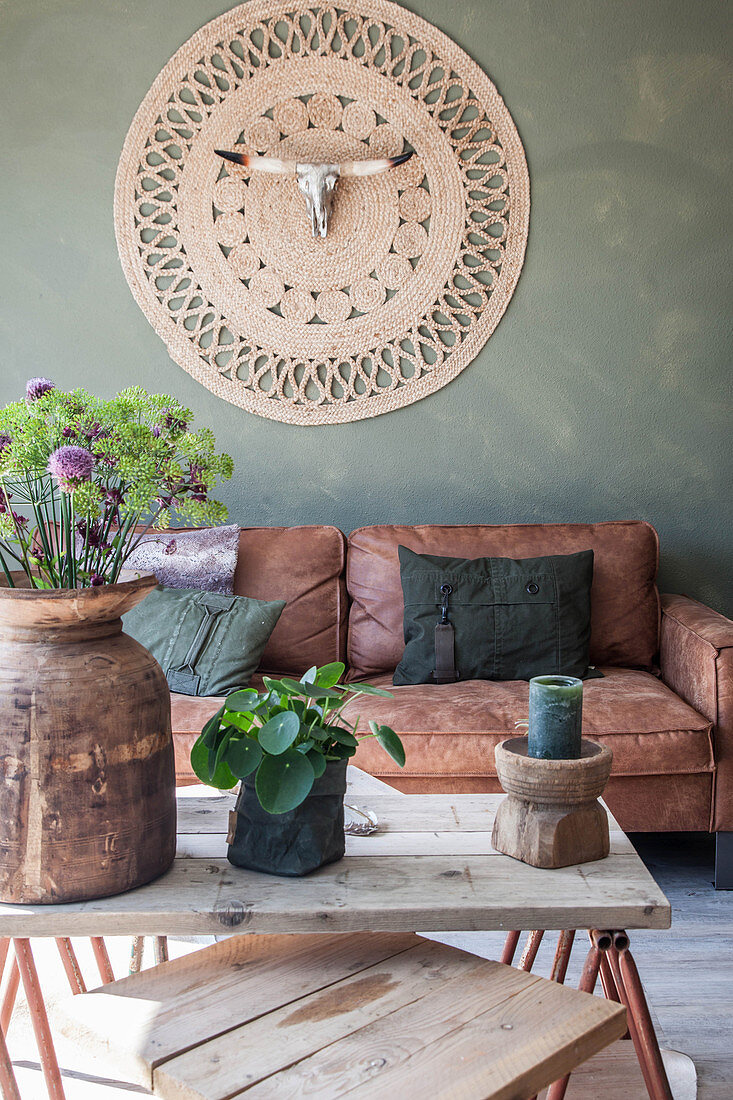 Coffee table, brown leather sofas and wall hanging with animal skull in living room with green wall