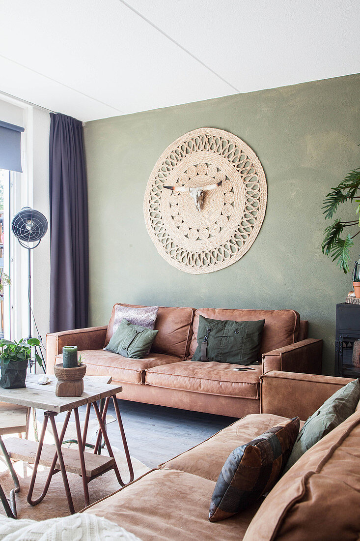 Ledersofas und Wandteppich mit Tierschädel im Wohnzimmer mit grüner Wand